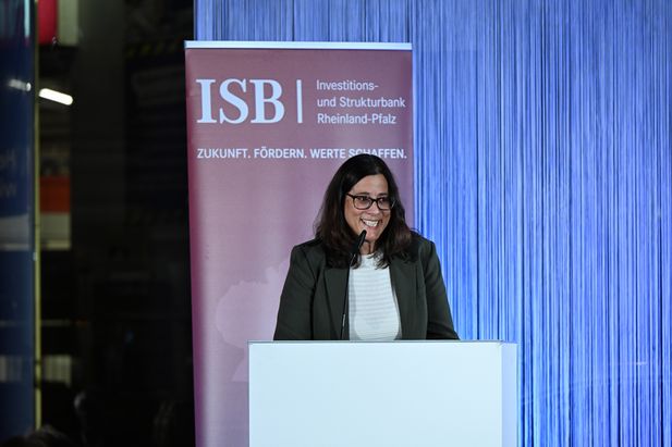 Person steht an einem Rednerpult vor einem Banner der Investitions- und Strukturbank Rheinland-Pfalz (ISB) mit dem Slogan ‚Zukunft. Fördern. Werte schaffen.