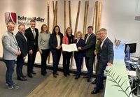 Eine Gruppe von Personen steht in einem modernen Bürobereich vor einer Wand mit Bambusdekor und dem Logo Bohr und Adler Notariat. In der Mitte hält die Gruppe ein geöffnetes Dokument. Rechts im Bild befindet sich ein Empfangstresen mit einem Monitor und einer Pflanze.