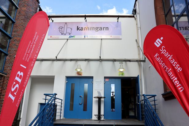 Der Eingang eines Gebäudes mit zwei blauen Eingangstüren und davor zwei rote Beachflags mit weißer Aufschriftt "ISB" und "Sparkasse Kaiserslautern".