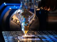 Laserauftragsschweißanlage bearbeitet eine Metallplatte. Aus der Bearbeitungseinheit treten helle Funken aus, während Metallpulver und Laserstrahlen eine Schutzschicht auf der Oberfläche erzeugen. Die Nahaufnahme zeigt den industriellen Beschichtungsprozess in einer Produktions- oder Forschungsumgebung.
