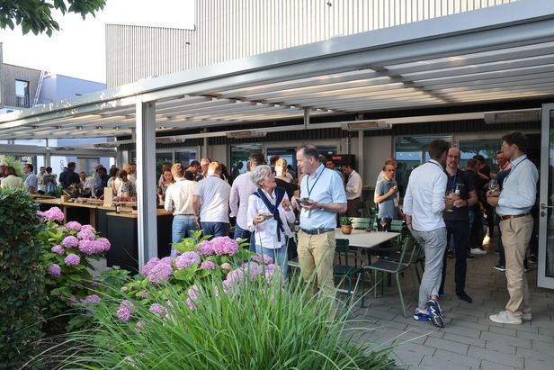 Menschen im Gespräch auf einer überdachten Terrasse mit Tischen, Stühlen und blühenden Hortensien im Vordergrund.