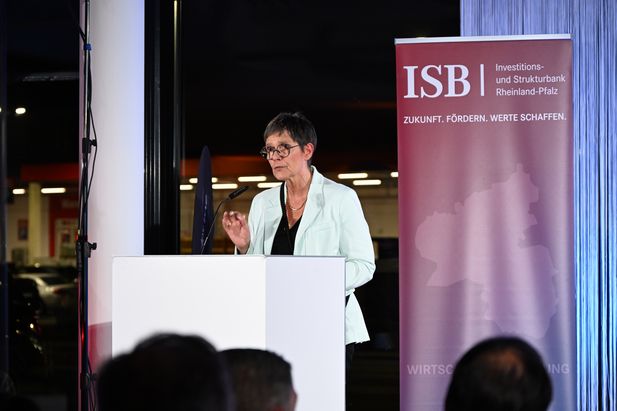 Person spricht an einem Rednerpult neben einem Banner der Investitions- und Strukturbank Rheinland-Pfalz (ISB) mit dem Slogan ‚Zukunft. Fördern. Werte schaffen