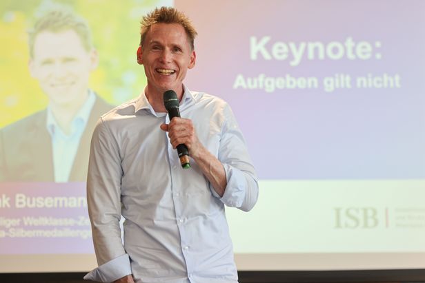 Person steht vor einer Pr&auml;sentationsfolie und spricht mit Mikrofon bei einer Veranstaltung; im Hintergrund ist eine Folie mit dem Wort &bdquo;Keynote&ldquo; zu sehen. 