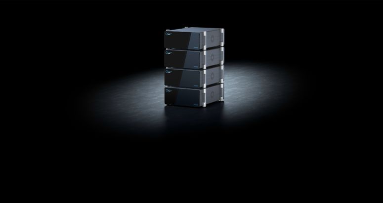 Vier &uuml;bereinandergestapelte, rechteckige elektronische Ger&auml;te-Module in dunklem Design, zentral auf einer dunklen Fl&auml;che stehend und von oben beleuchtet.