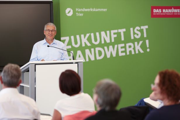Älter Mann an einem Rednerpult. Im Hintergrund eine grüne Leinwand mit Aufschrift "Zukunft ist Handwerk".