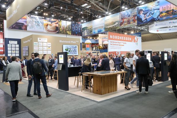 Messestand mit den Aufschriften „Rheinland-Pfalz“ und „NORDHESSEN“ auf einer Fachmesse. Zahlreiche Personen stehen vor Infotafeln und unterhalten sich. Im Hintergrund sind Banner mit Landschaftsmotiven und Firmenlogos zu sehen.