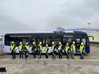 Gruppe von Personen mit Sicherheitswesten und Helmen steht mit Spaten vor einem Linienbus des Nahverkehrsverbunds auf einer Baustelle