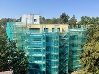 Mehrgeschossiges Studentenwohnheim in Kaiserslautern mit großflächigem Baugerüst und grünem Schutznetz. Das Gebäude ist von Bäumen umgeben, die Sanierungsarbeiten an der Fassade sind deutlich sichtbar.