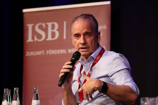 Ein Mann mit Mikrofon spricht auf einer Bühne vor einem ISB-Banner mit der Aufschrift ‚Zukunft, Fördern, Werte schaffen.