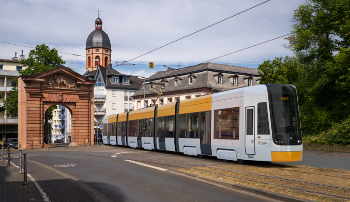Moderne gelb-wei&szlig;e Stra&szlig;enbahn f&auml;hrt durch das Gautor in Mainz, im Hintergrund historische Geb&auml;ude und ein Kirchturm.
