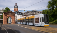 Moderne Straßenbahn fährt durch das historische Gautor in Mainz; im Hintergrund sind Wohnhäuser und ein Kirchturm zu sehen.