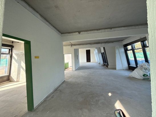 Rohbau&auml;hnlicher Innenbereich eines Studentenwohnheims mit freiger&auml;umten R&auml;umen, sichtbaren Betondecken und gro&szlig;en Fensterfl&auml;chen. Die Fl&auml;che befindet sich w&auml;hrend laufender Sanierungsarbeiten im Umbau.