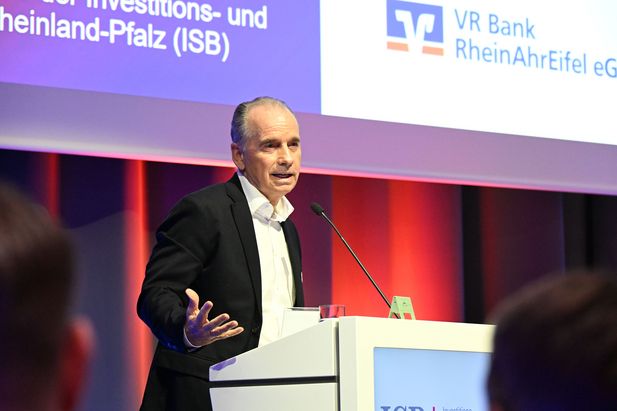 Person h&auml;lt einen Vortrag an einem Rednerpult vor einer Pr&auml;sentationsleinwand mit Logos von ISB und VR Bank RheinAhrEifel.